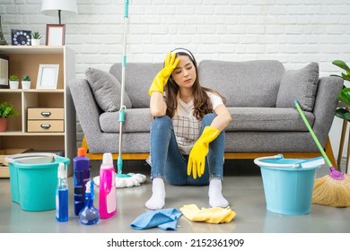 Beautiful Asian housewife feeling tired after doing housework. She sits on the floor in the living room with home cleaning products.