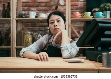 Beautiful Asian Korean Pensive Barista In Apron Leaning On Bar Counter Table In Vintage Coffee Shop. Startup Business Not Successful Concept. Lady Cafe Owner Bored Waiting Customer To Come Cafeteria