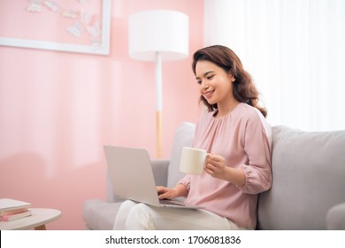 Beautiful Asian Lady Working On Laptop At Home, Sitting On Couch