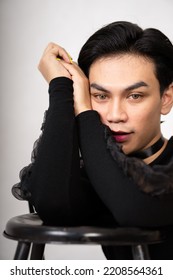 beautiful Asian man posing with the chair while wearing a black costume and makeup inside the white studio - Shutterstock ID 2208564361