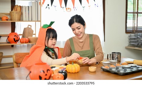 Beautiful Asian Mom And Her Cute Daughter Baking Halloween Pumpkin Cupcakes Together At Home. Halloween Activity Concept