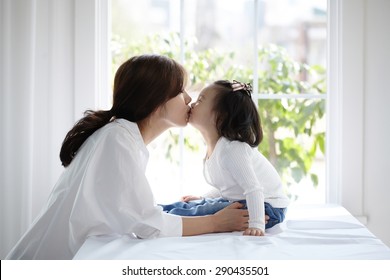 Beautiful Asian Mom And Her Cute Daughter Kissing With Love While Looking At Each Other

