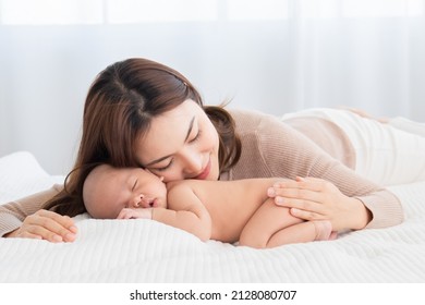 Beautiful Asian Mom Supports And Tenderly Cuddles Newborn Baby Gently While Baby Sleeping. Young Woman Kissing And Touching On Back Child With Love And Tender. Mother And Infant Spend Time Together.