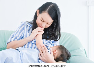 Beautiful Asian Mother Breastfeeding Her Son On Sofa At Home.