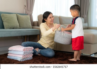 Beautiful Asian Mother And Child Boy Little Helper Are Having Fun And Smiling While Doing Help Her Mother Folded Clothes Laundry At Home. Happy Family.
