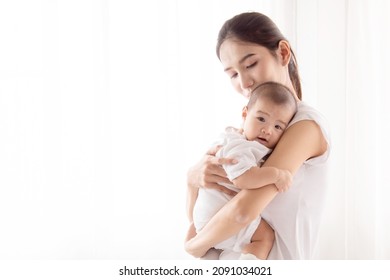 Beautiful Asian Mother Hold And Embrace Her Todlder, Mom Looking Her Baby With Love And Tender, Infant Looking At Camera. Relax Enjoy Tender Family Moment At Home.