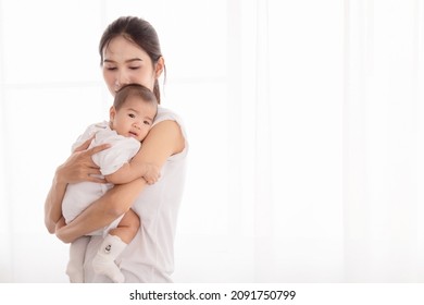 Beautiful Asian Mother Hold And Embrace Her Todlder, Mom Looking Her Baby With Love And Tender. Mother Holding Newborn Baby In Arms And Support Baby Back By Her Hand. 