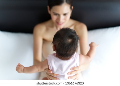 Beautiful Asian Mother Holding Baby On The Bed. Seen From Behind Baby And Selective Focus On Baby's Head. Mother Is Feeling Love And Smiling To Her Kid. Love And Relation Bond Of Mother And Child.