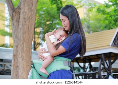 Beautiful Asian Mother Hugging Her Infant On Ergonomic Baby Carrier In The Garden.