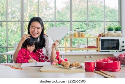 Beautiful Asian mother   mixed race adorable little daughter sitting in kitchen  drawing  painting  doing homework activities   making card Valentine day together  smiling and happiness