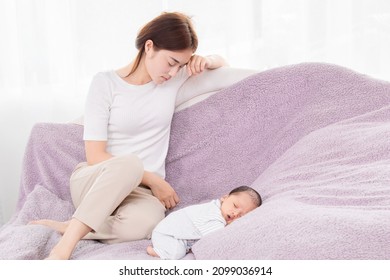 Beautiful Asian Mother Sitting Sleepy Next To Baby, Single Mom Exhausted From Raising Children. Newborn Sleeping With His Head Laying In His Tiny Hands.