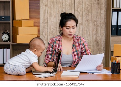 Beautiful Asian Mother Woman Taking Care Baby Multi Task Working At Home Using Laptop, Smartphone Packing Products Cardboard, Small Business Startup Entrepreneur, Freelance Lifestyle Shopping Online