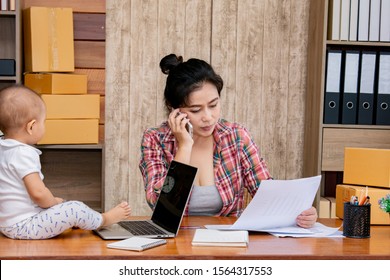 Beautiful Asian Mother Woman Taking Care Baby Multi Task Working At Home Using Laptop, Smartphone Packing Products Cardboard, Small Business Startup Entrepreneur, Freelance Lifestyle Shopping Online