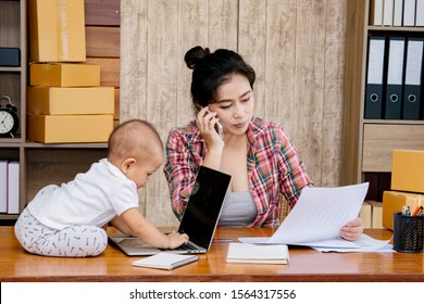 Beautiful Asian Mother Woman Taking Care Baby Multi Task Working At Home Using Laptop, Smartphone Packing Products Cardboard, Small Business Startup Entrepreneur, Freelance Lifestyle Shopping Online