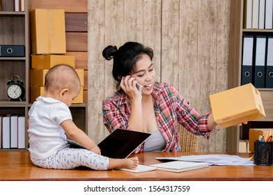 Beautiful Asian Mother Woman Taking Care Baby Multi Task Working At Home Using Laptop, Smartphone Packing Products Cardboard, Small Business Startup Entrepreneur, Freelance Lifestyle Shopping Online