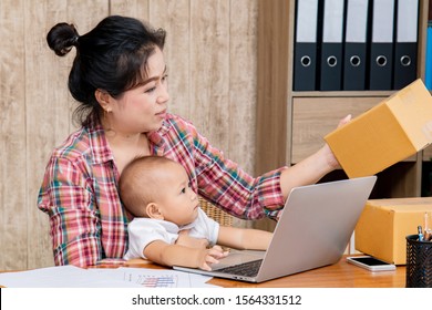 Beautiful Asian Mother Woman Taking Care Baby Multi Task Working At Home Using Laptop, Smartphone Packing Products Cardboard, Small Business Startup Entrepreneur, Freelance Lifestyle Shopping Online