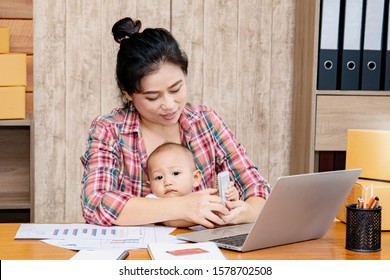 Beautiful Asian Mother Woman Taking Care Baby Multi Task Working At Home Using Laptop, Smartphone Packing Products Cardboard, Small Business Startup Entrepreneur, Freelance Lifestyle Shopping Online