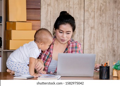 Beautiful Asian Mother Woman Taking Care Baby Multi Task Working At Home Using Laptop, Smartphone Packing Products Cardboard, Small Business Startup Entrepreneur, Freelance Lifestyle Shopping Online