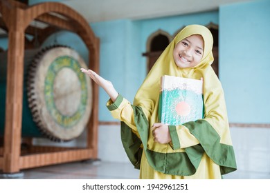 beautiful asian Muslim girls smiling holding al quran book in hands and showing something
