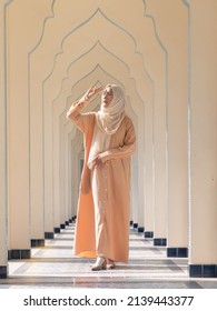 Beautiful Asian Muslim Woman Wearing Earth Tone Color Abaya And Hijab Dress Putting Hand To Block Sun Rays While Walking In The Beautiful Alley.