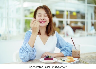 A beautiful Asian portrait is taking a spoonful of cakes on the table and eating them with happy eyes and expressions in the bakery.