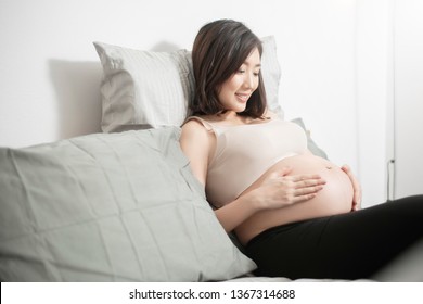 Beautiful asian pregnant woman lying on her bed, touching  big belly  - Powered by Shutterstock