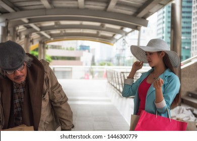 Beautiful Asian Rich Woman With Many Shopping Bag Look Down And Mean To Beggar Or Homeless Old Man In Urban City. Bad Habit For High Society Or Gentility To Disgust The Poor.