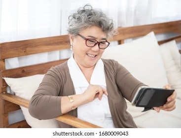 Beautiful asian senior elder woman in casual clothes making  selfie using smart phone and smiling while sitting on couch in living room at home - Powered by Shutterstock