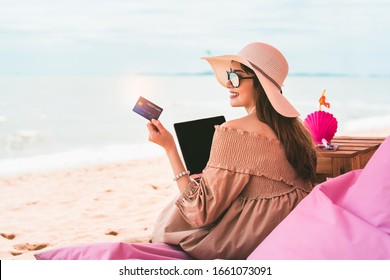 Beautiful Asian Smile Woman Relax At Beach On Summer Vacation. Holding Credit Card With Computer. Digital Payment Concept For Shop Online And Booking Hotel When Travel. Pattaya, Thailand.