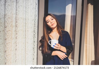 Beautiful Asian smiling woman enjoying coffee or tea on sunny balcony. Young happy lady in blue bathrobe chilling sunbathing on terrace at summertime - Shutterstock ID 2126874173