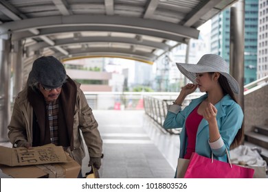 Beautiful Asian Tourist Woman With Many Shopping Bag Look Down On Smell Beggar Or Homeless Dirty Old Guy In Urban City. Bad Habit For High Society Or Gentility To Disgust The Poor.