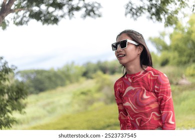 beautiful Asian trans woman wearing a red and white striped shirt and sunglasses. In a green park on a sunny day. - Powered by Shutterstock