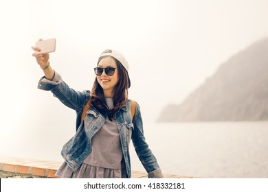 Beautiful Asian traveler taking selfie with ocean view background, soft warm light tone