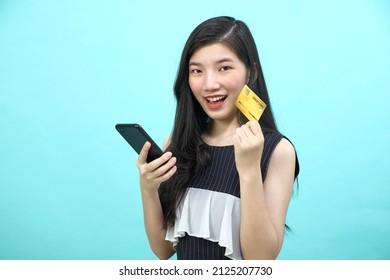 Beautiful Asian womฟn use smartphone and credit card payments online shopping online on light blue studio isolated background