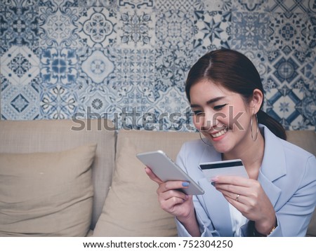 Beautiful Asian using her mobile to do internet banking, online shopping while she holding credit card in another hand. Paypal concept. Internet Banking concept.