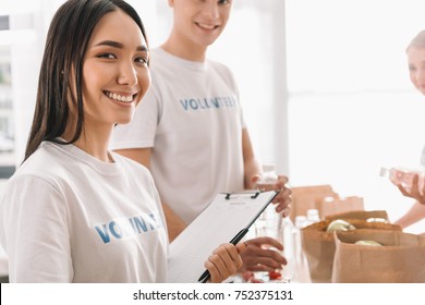 Beautiful Asian Volunteer Girl With Clipboard And Blurred Colleagues On Background