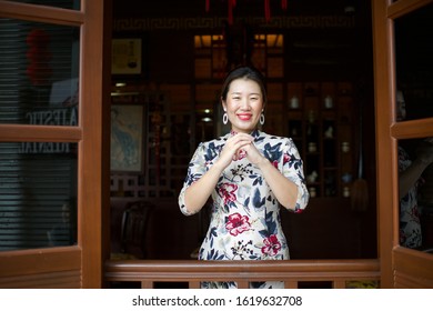 Beautiful Asian waitress doing welcome gesture in the restaurant window.Chinese New Year celebration greeting.Female working in hotel.Oriental setting lobby.Woman wearing qipao.