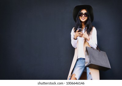 Beautiful Asian well-dressed young irl holding a  brown blank paper bag and makes purchases in an online store against a black wall background with copy space for text or design. Horizontal mockup