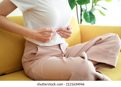 Beautiful Asian woman with abdominal pain in the middle above the navel. She sits on the sofa at home. Concept of treatment of pancreas, stomach, gallbladder or esophagus in women. health care
