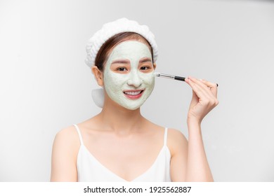 Beautiful Asian woman applying clay mask on her face isolated over white background.