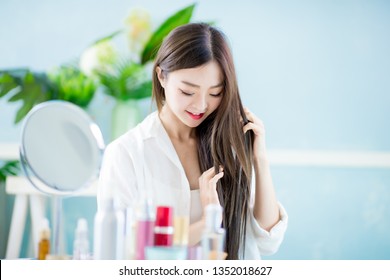 Beautiful Asian Woman Applying Oil Onto Hair With Mirror At Home