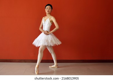 Beautiful Asian Woman Ballet Dancer Practice Dance Jump Move Wearing Tutu At Home Red Orange Background Wall