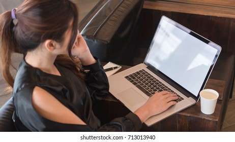 Beautiful Asian Woman In Black Dress Working With Laptop In Coffeeshop, Blank Screen Computer For Mock Up Template Or Screen In Sertion
