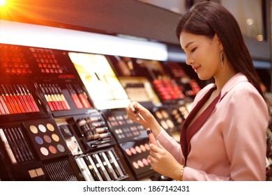 Beautiful Asian Woman In A Business Pink Suit Is Selecting And Shopping Cosmetic In Department Store, Copy Space Selective Focus