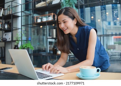 Beautiful Asian woman in casual blue shirt using laptop at cafe, Happy Freelancer woman working with laptop. - Powered by Shutterstock