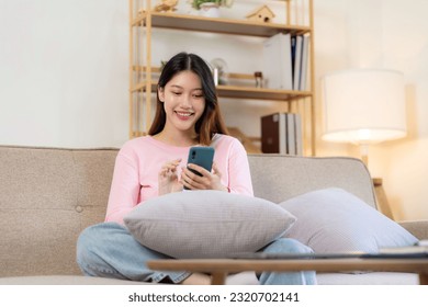 Beautiful Asian woman in casual clothes sitting on sofa using smartphone for social entertainment to relax. smile and laugh - Shutterstock ID 2320702141