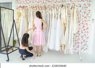 Beautiful Asian Woman Choosing Wedding Dress With Assistant Designer Wedding Dresses, Measures The Dress On Her Fitting In Bridal Clothing Shop Before The Special Day Of Her. Dealer Consultant Concept