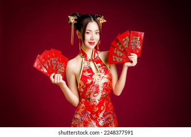 Beautiful Asian woman with clean fresh skin wearing traditional cheongsam dress holding red envelopes or Ang Pao on red background. Happy Chinese new year. Chinese text means great luck great profit. - Shutterstock ID 2248377591