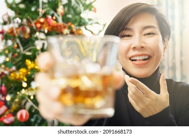 A Beautiful Asian Woman With Cocktail Drinks In Hand Smiling To Web Cam Video Call For Online Party With Her Friends On Christmas Eve 2022, New Normal, Technology, Happiness, New Year's Eve Countdown.