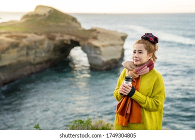 Beautiful Asian Woman With Coffee Cup During Sunrise At Tunnel Beach, Otago Peninsula, New Zealand.